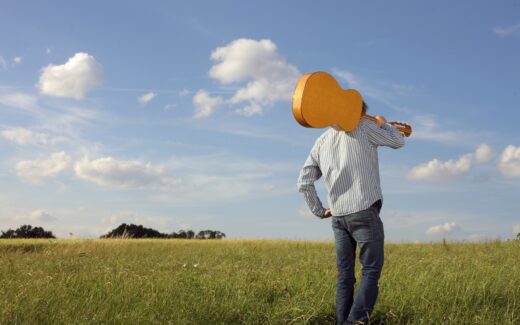 man met gitaar op zijn schouder loopt door weids boerenland